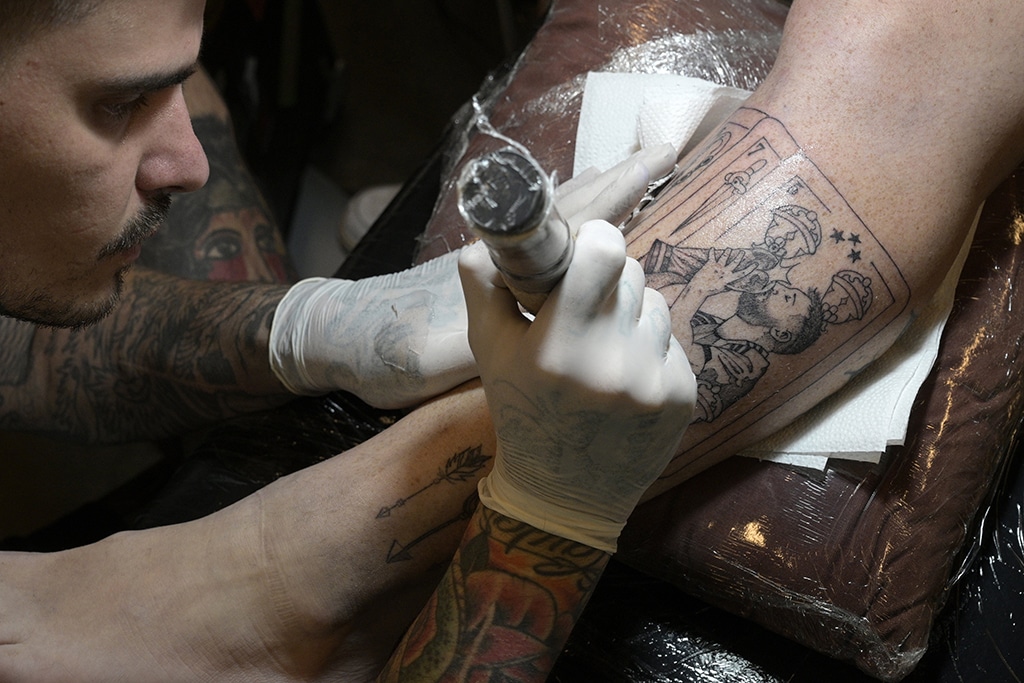 Argentine tattooist Tebi Cobra Vucinovich works on a tattoo of Argentina's forward Lionel Messi kissing the FIFA World Cup trophy on the leg of Ariel Sacchi at Ds Tattoo Shop in Buenos Aires on Dec 23, 2022. – AFP photos