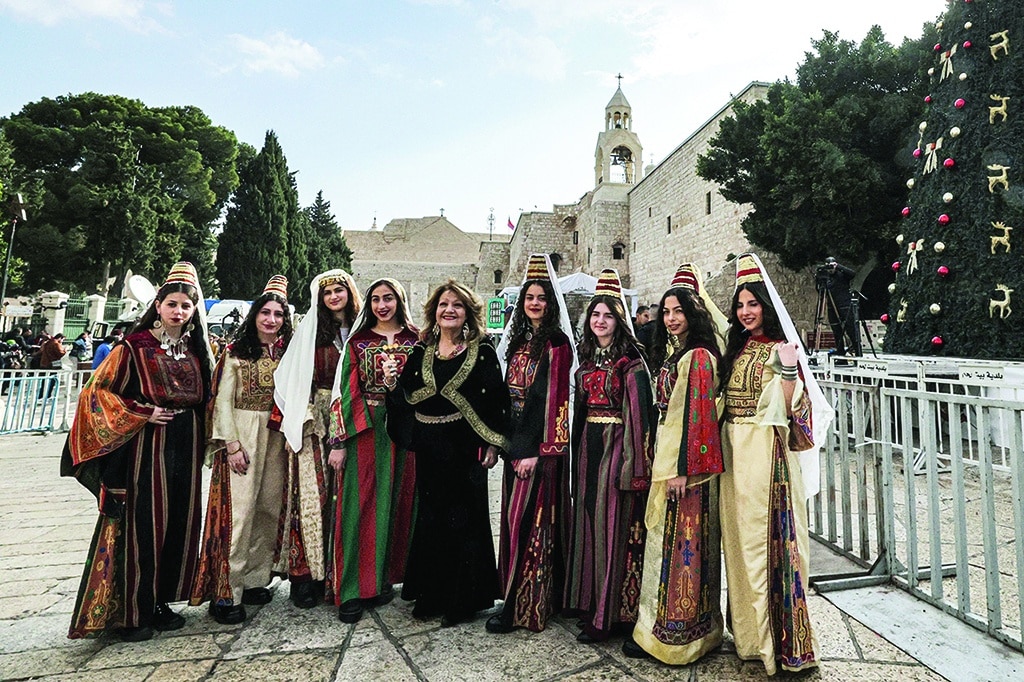 BETHLEHEM: Women dressed in traditional clothing pose for a picture by a Christmas tree in Manger Square outside the Church of the Nativity in this biblical city in the occupied West Bank on Dec 24, 2022. - AFP