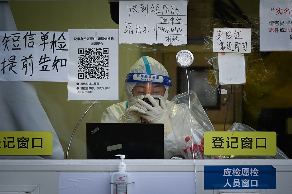 BEIJING: A health worker uses her phone as she waits for people at a nucleic acid testing booth on Dec 27, 2022. - AFP