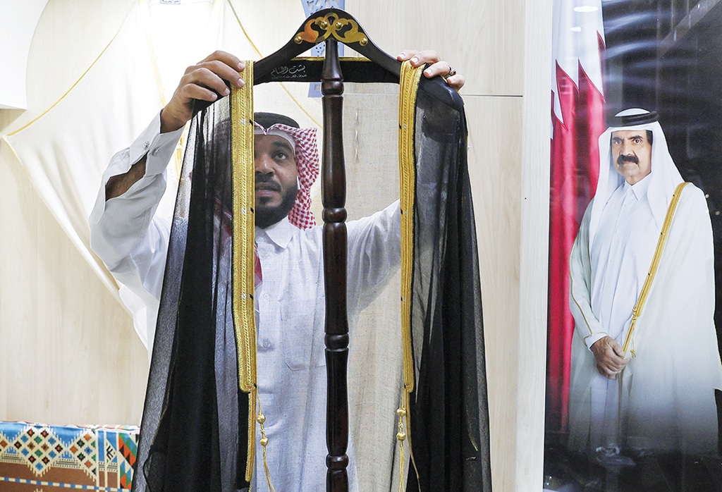 DOHA: A Qatari man works on a traditional black and gold Arab cloak (bisht) in front of a portrait of Qatar's former Amir Sheikh Hamad Bin Khalifa Al-Thani, at the Al Salim store in Doha's Souq Waqif market.- AFP