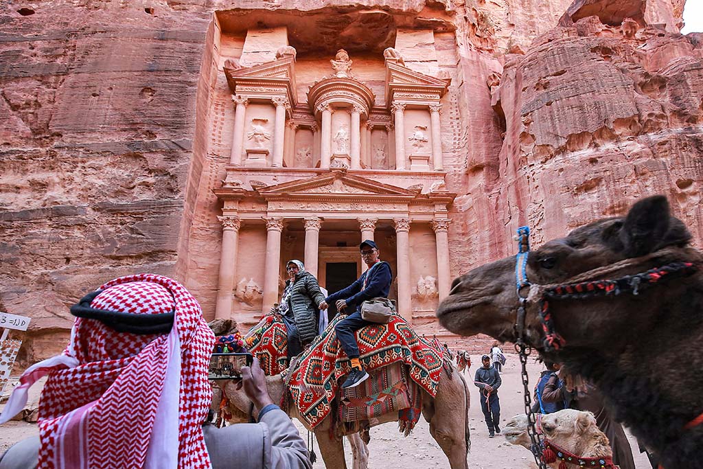 A tourist poses for a photo while riding a camel before the site of the Treasury at the ruins of the ancient Nabatean city of Petra. 