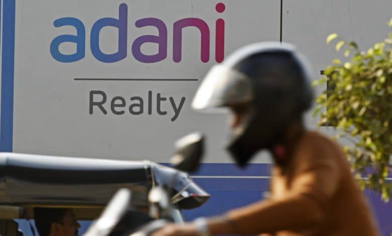MUMBAI: A man wearing a helmet passes by an advertisement board of Adani Reality in Mumbai.