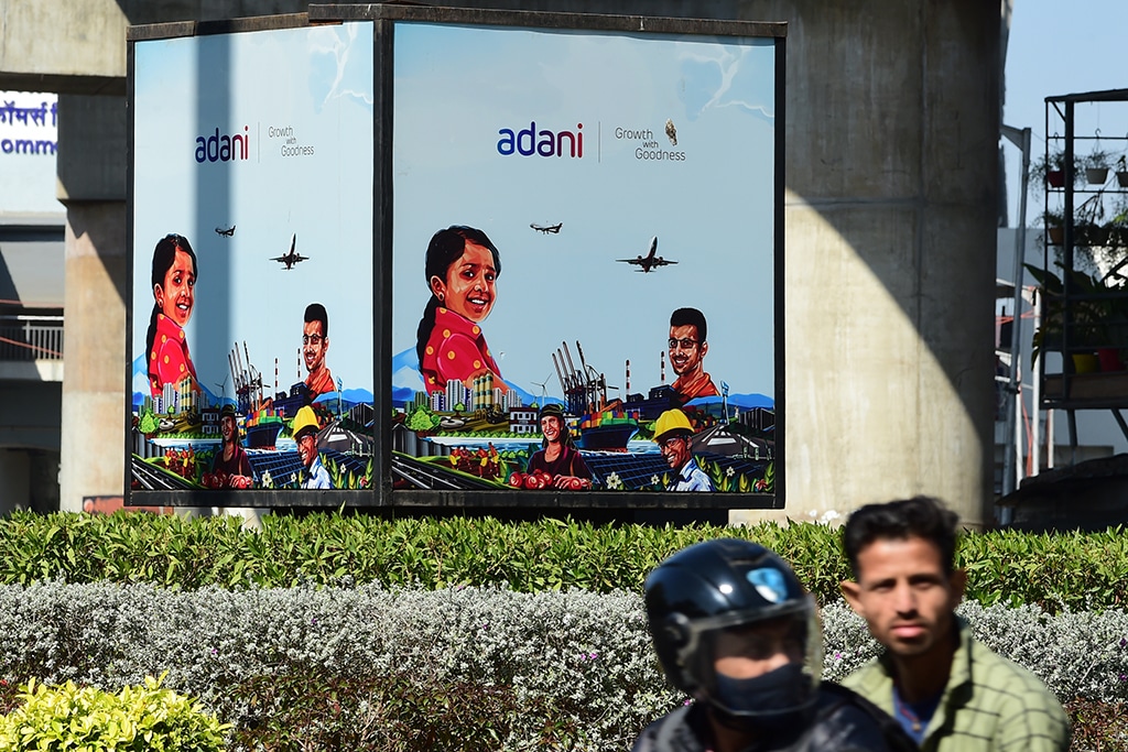 AHMEDABAD: Men ride a motorbike past an Adani Group advertisement billboard in Ahmadabad. - AFP