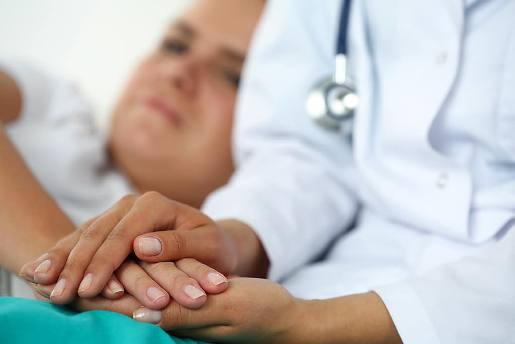 Friendly female doctor hands holding patient hand lying in bed for encouragement, empathy, cheering and support while medical examination. Bad news lessening, compassion, trust and ethics concept