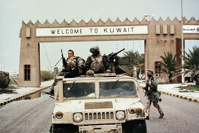 In this Feb 27, 1991 file photo, members of Task Force Ripper of the First Marine Division ride a Humvee under a “Welcome to Kuwait” sign at the entrance to Kuwait City’s International Airport.
