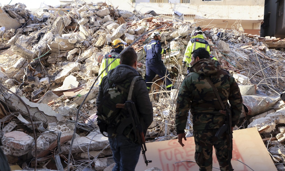 Syrian soldiers look on as Emirati rescuers search for victims amidst the rubble of a collapsed building in the regime-controlled town of Jableh in the province of Latakia, northwest of the Syrian capital, on February 10, 2023.
