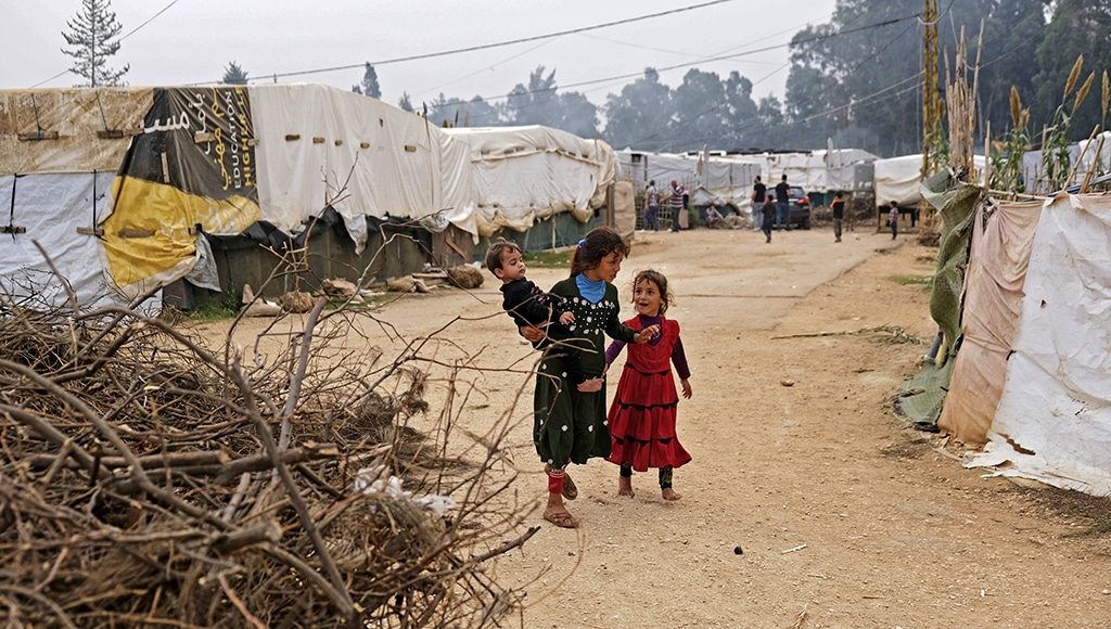 AKKAR: A girl speaks with another as he carries a young boy while walking past tents at a make-shift camp for Syrian refugees in Talhayat in the Akkar district in north Lebanon.- AFP