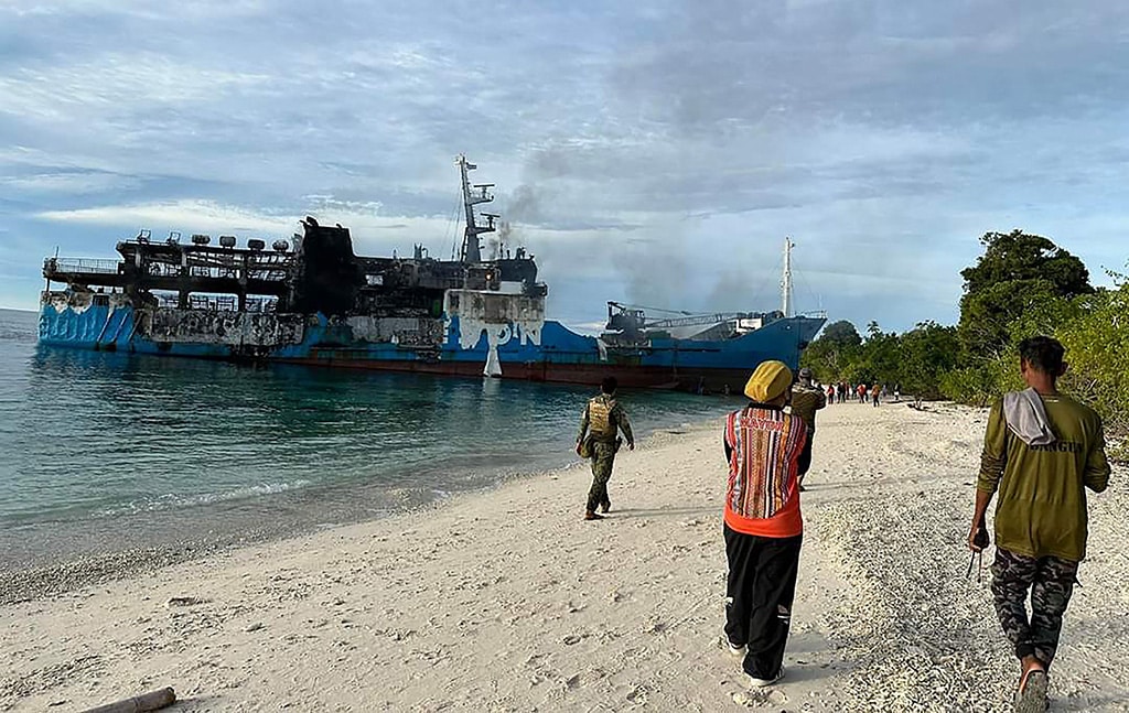 HADJI MUHTAMAD, Philippines: This handout photo taken on March 30, 2023 shows people walking towards the burnt passenger ferry Lady Mary Joy 3 after it was towed to the shore in Basilan province. - AFP