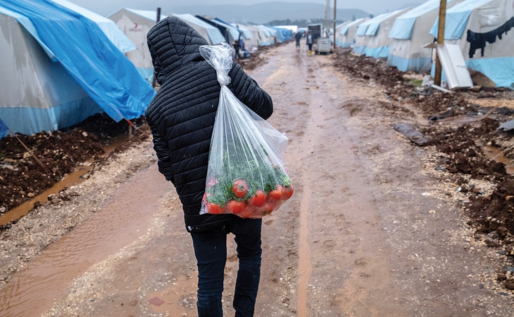 ADIYAMAN: A displaced man carries a sack of tomatoes as he walks under the rain past tents set up to home displaced people following a massive earthquake in Adiyaman, southeastern Turkey.- AFP