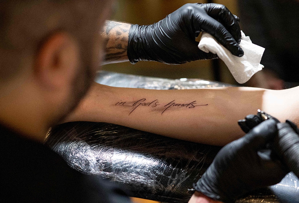 Tattoer Silas Becks puts protective patch over a tattoo reading 'In God's hands..' on the arm of a young man in Vienna, Austria.--AFP photos