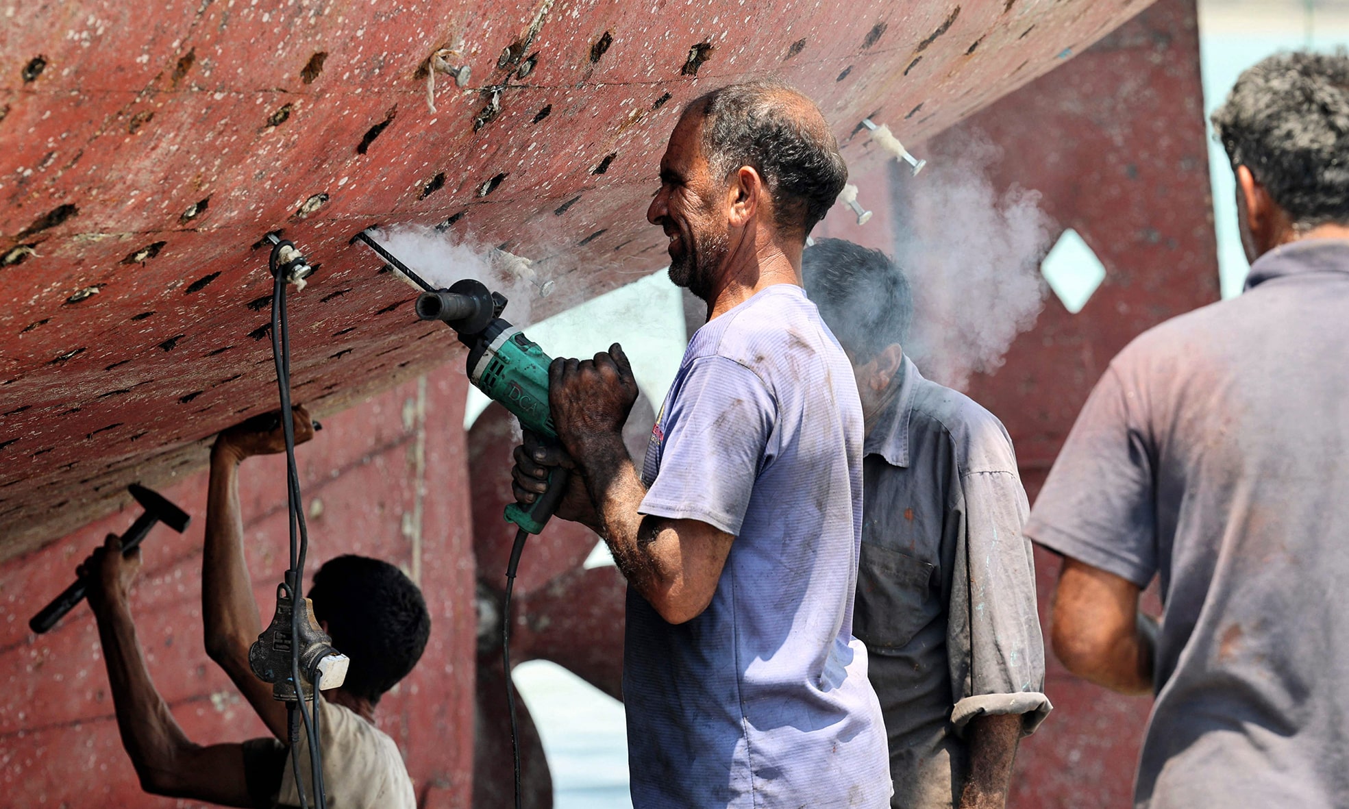 Workers restore a traditional wooden ship (lenj) in a shipyard.