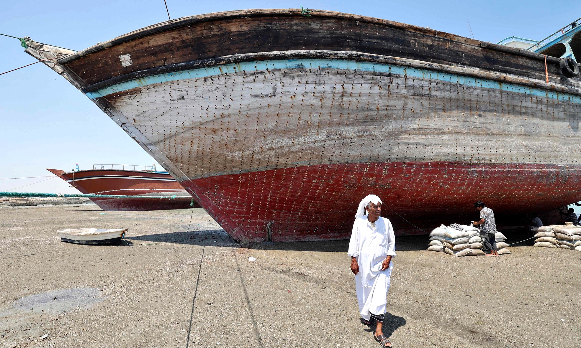 A man walks in front of a traditional wooden ships (lenj).