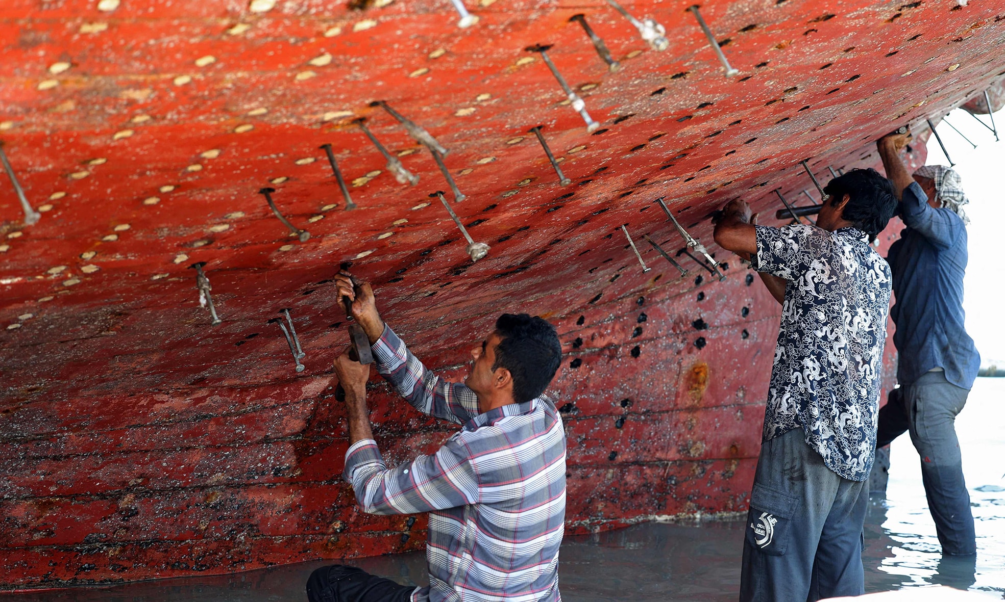 Workers restore a traditional wooden ship (lenj) in a shipyard.
