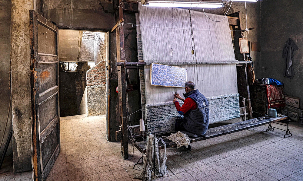 A worker operates a loom while fabricating a rug at the Kahhal looms hand-made rugs workshop in the Basatin district of Cairo.