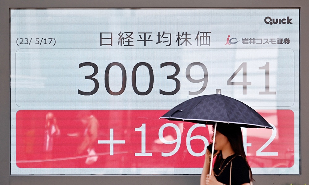 TOKYO: A woman walks past an electronic quotation board displaying the 225-issue Nikkei Stock Average (top) on a street in Tokyo on May 17, 2023. --AFP