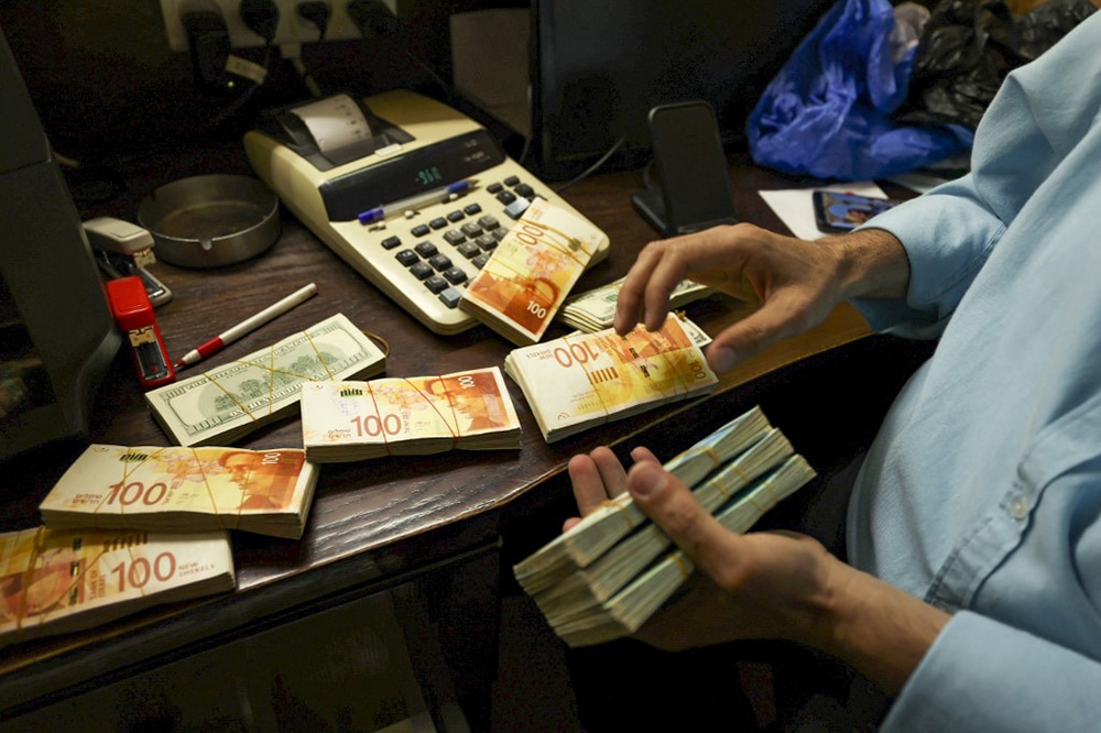 A Palestinian man counts stacks of banknotes at a currency exchange counter in the West Bank city of Ramallah. -- AFP