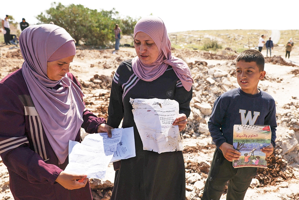 JABBET AL-DHIB: Palestinians pick up papers and books from the site of a school that was demolished by Zionist authorities in this village east of Bethlehem in the occupied West Bank on May 7, 2023. – AFP