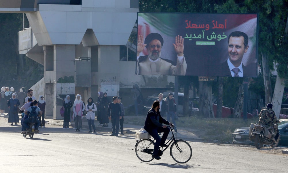 A billboard with pictures of Iranian President Ibrahim Raisi (L) and Syrian President Bashar al-Assad stands on the road in Damascus on May 3, 2023.