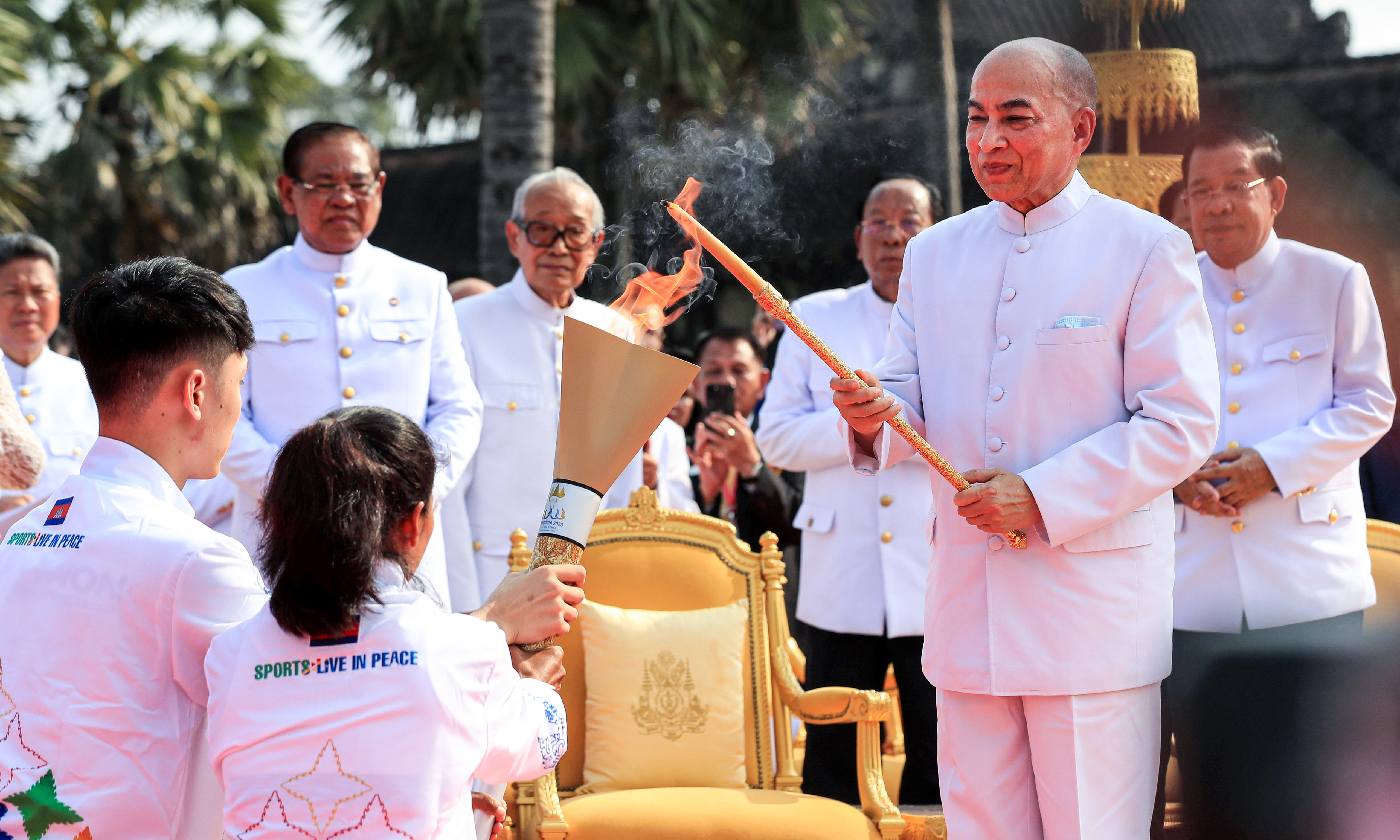 SIEM REAP PROVINCE: Cambodiaís King Norodom Sihamoni (2nd right) lights the torch with a candle lit from the sunís rays as Prime Minister Hun Sen (right) looks on during a ceremony prior to the 32nd SEA Games at Angkor Wat temple in Siem Reap province.- AFP