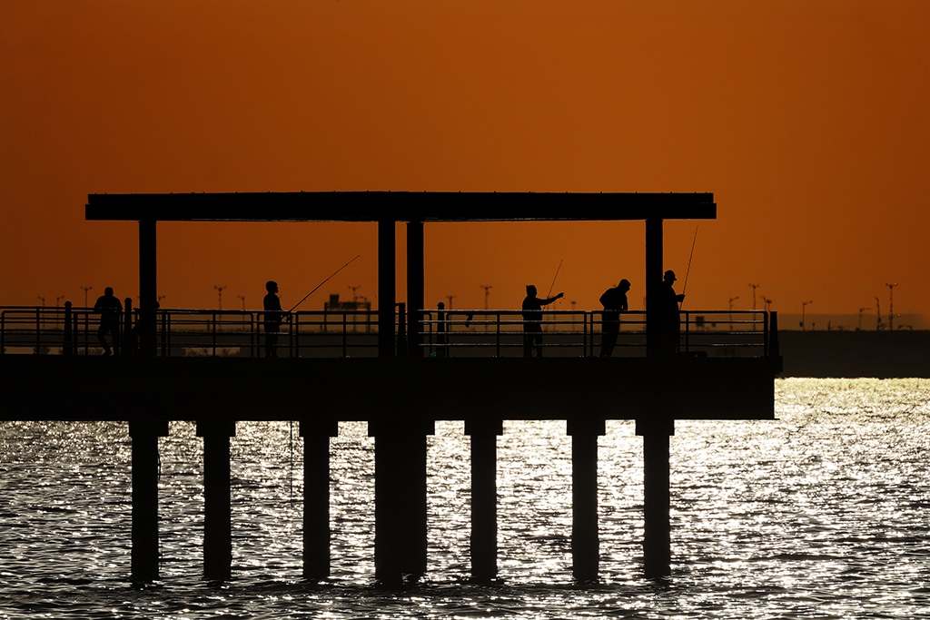 KUWAIT: People are seen fishing on a pier overlooking the glistening Arabian Gulf at sunset. The pier is located near Souq Sharq, a shopping center in Kuwait City. — Photo by Yasser Al-Zayyat