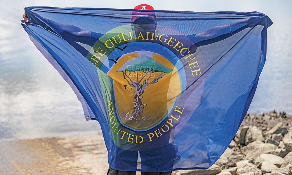 A Gullah Geechee man holds up an official flag of the Gullah Geechee people at Station Creek Landing in St Helena, South Carolina.