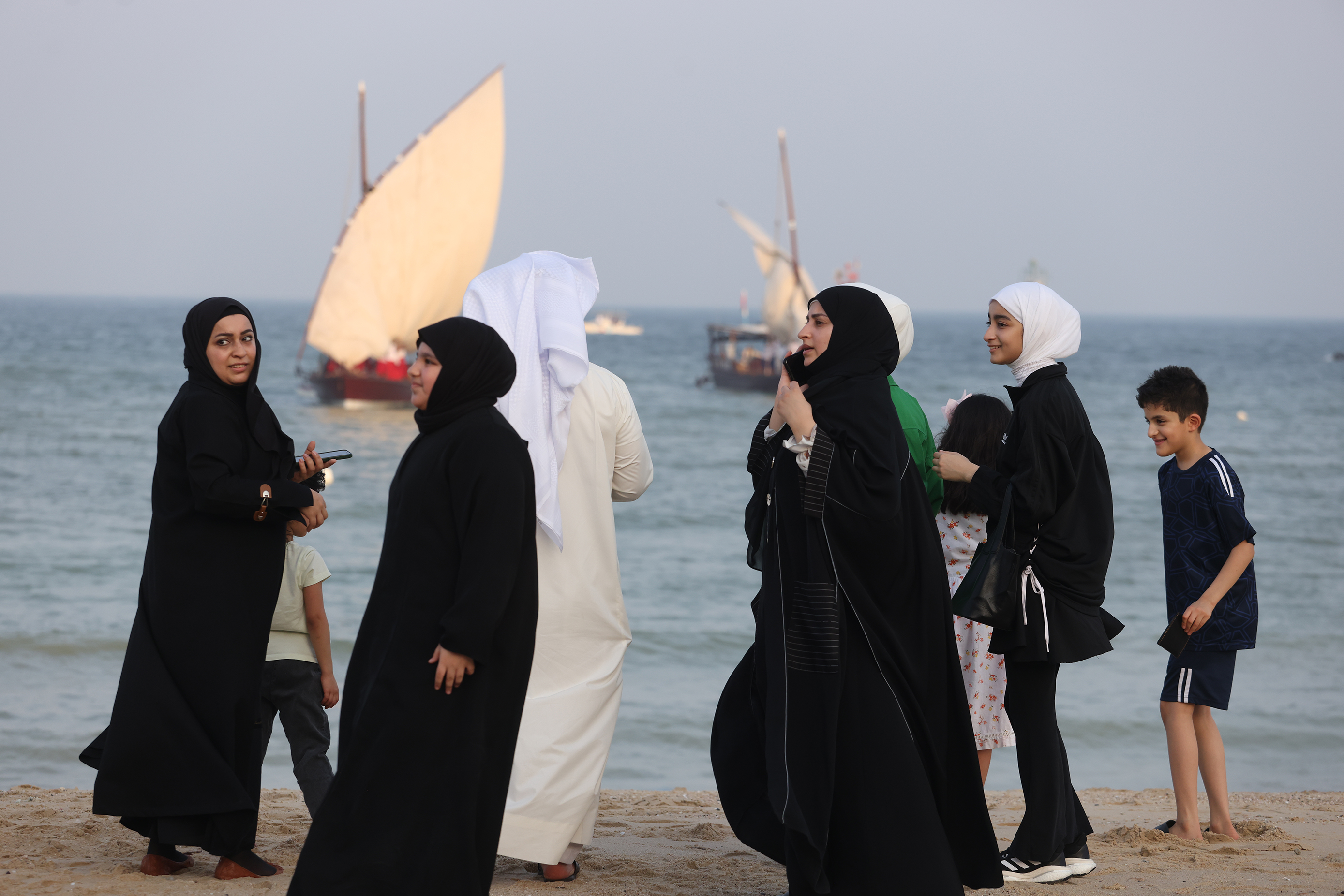 Family members of a Kuwaiti youth wave as traditional dhows prepare to sail for a pearl diving expedition from the shore of Kuwait City.