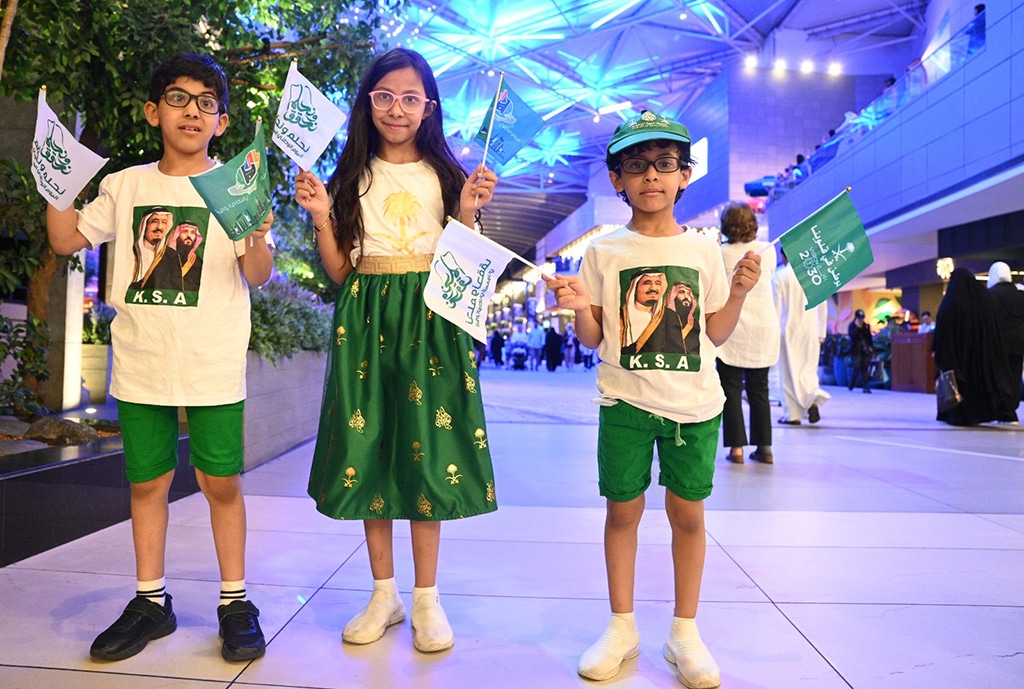 Children wave Saudi national flags on the occasion.