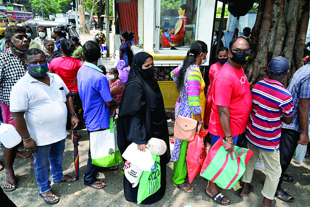 COLOMBO: People stand in a queue to buy kerosene oil for home use at a petrol station in Colombo.-AFP